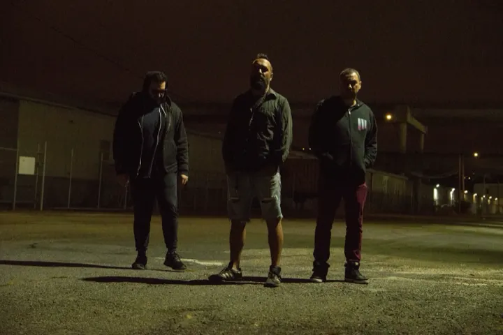 Three band members standing in an empty lot at night