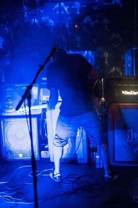 A band member on stage among amplifiers, washed in blue light